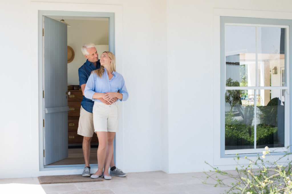 Happy,Mature,Couple,Embracing,In,Front,Of,The,Door.,Smiling